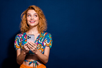 Photo of pretty young woman hold phone look empty space wear top isolated on dark blue color background