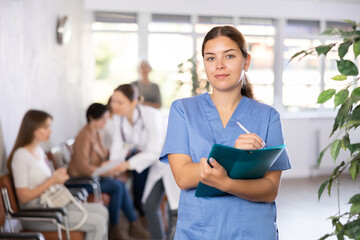 Young woman in medical uniform making notes in notebook at reception