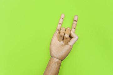 A wooden hand on a green paper background shows two fingers, index and little finger, horn (stone) gesture. Concept of love, approval and admiration. Artificial intelligence.