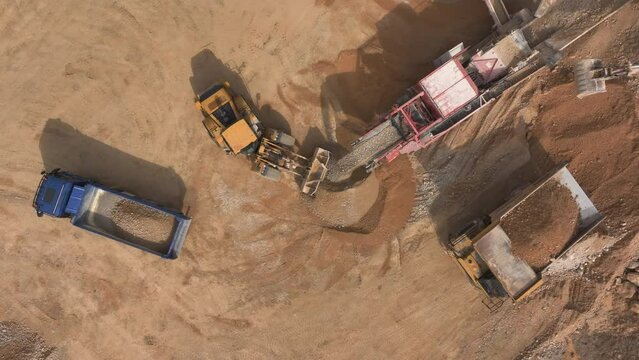 Zoom out aerial shot - Gravel falling off of conveyor belt in a quarry and excavator loading it up onto a dump truck