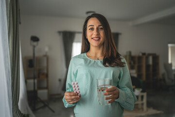Adult pregnant women stand and hold medicament glass of water at home