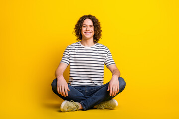 Full size portrait of nice young man sit floor wear striped t-shirt isolated on yellow color...