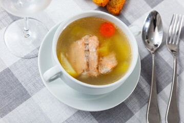 Appetizing rich salmon backbone soup with potatoes and carrots served in white tureen with crispy toasts .. - obrazy, fototapety, plakaty