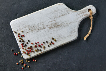White wooden cutting board and multi-colored peppercorns on a black concrete table