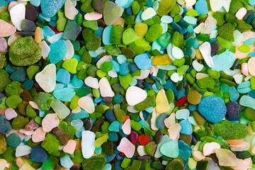 Multi-colored fragments of glass bottles polished by the sea scattered on the background