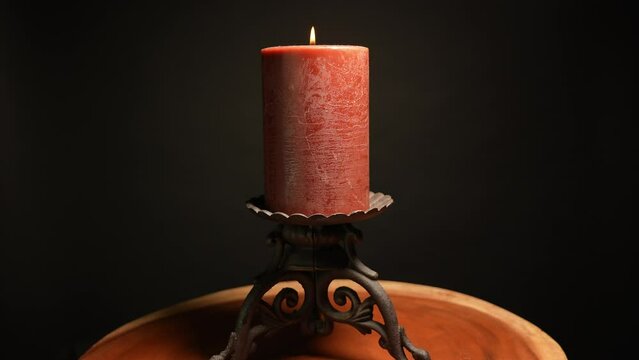 Ancient old red candle light burning on medieval gothic candlelight holder. Black background and wooden cross cut tree trunk.
