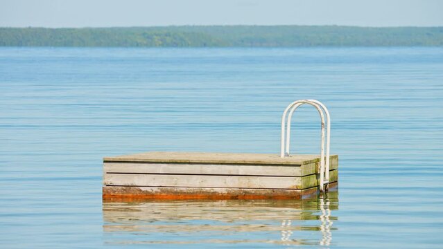 Floating swim platform in the lake, anchored in place and used for kids and people to jump into the water. Swimming floating platform or diving board drifting at Lake Manitou, Manitoulin Island.