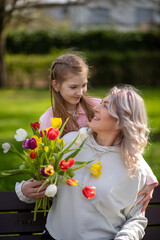 Daughter gives mother tulips, both smiling outdoors
