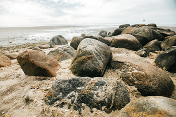 Fototapeta na wymiar Stone boulders on the beach at low tide.Wadden Sea Coast.Stone groyne close-up on cloudy sky background.. Marine photo wallpaper.Nature of the North Sea coast. 