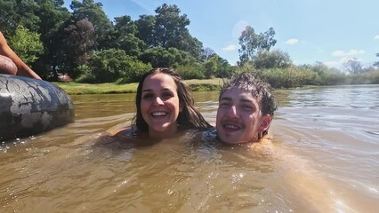 Selfie, swimming and couple in lake for fun on holiday, summer vacation and weekend. Live streaming, camp and portrait of man and woman on adventure for content creation, vlog and travel influencer - Powered by Adobe