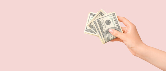 Female hand holding one hundred dollar banknotes on pink background