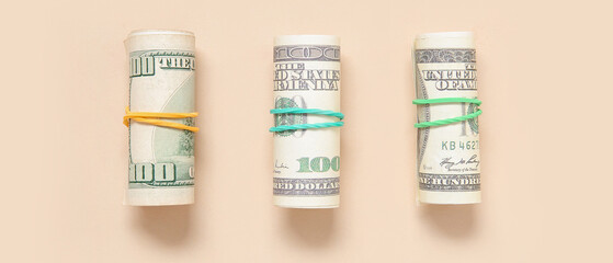 Rolls of one hundred dollar banknotes tied with rubber bands on beige background