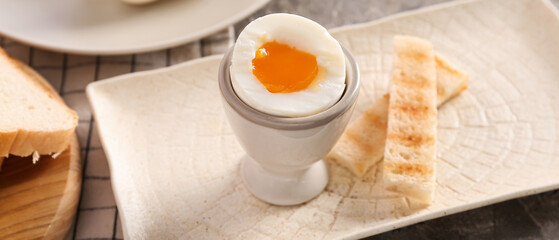 Holder with soft boiled egg and toasted bread on grey table