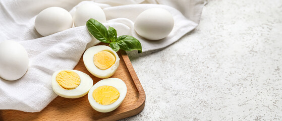 Wooden board with halves of boiled chicken eggs on light background, closeup