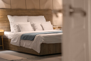 View of bed with pillows and blankets through open door in evening