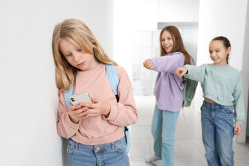 Bullied little girl using mobile phone near wall at school hall - obrazy, fototapety, plakaty