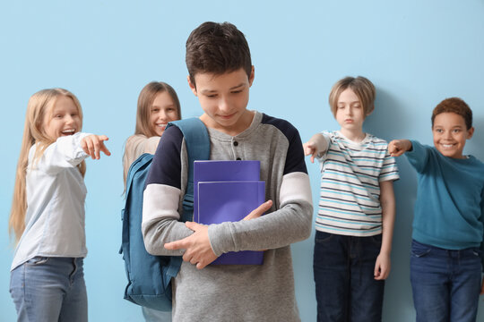 Bullied little boy with copybooks and pupils on blue background