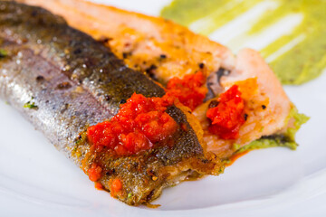 Portion of baked trout fillet with guacamole and tomato sauce