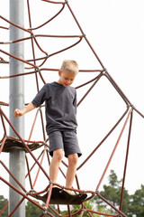 A happy boy is playing on a rope playground outdoors. A child climbs a rope net in the park.