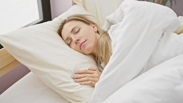 A serene young woman sleeps peacefully in a cozy bedroom, wrapped in white linens, depicting relaxation and comfort.
