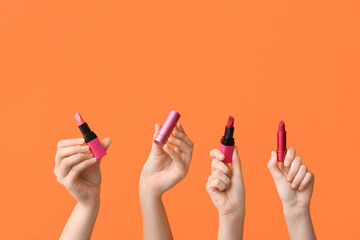 Female hands with lipsticks on orange background