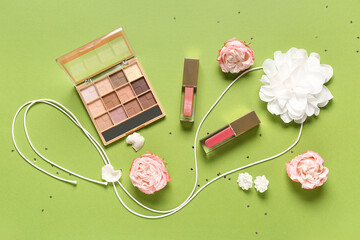 Eyeshadows palette with lip glosses, accessories and roses on green background
