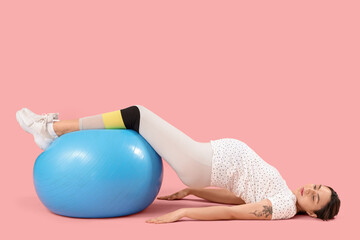 Beautiful young pregnant woman training with fitball on pink background