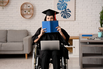 Beautiful female graduate student in wheelchair with graduation cap, laptop and book studying...