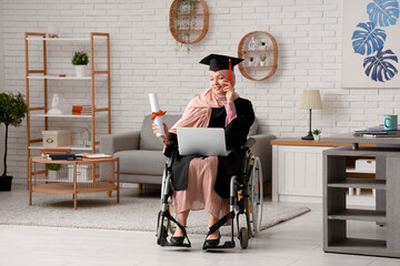 Beautiful female Muslim graduate student in wheelchair with graduation cap, laptop and diploma at...