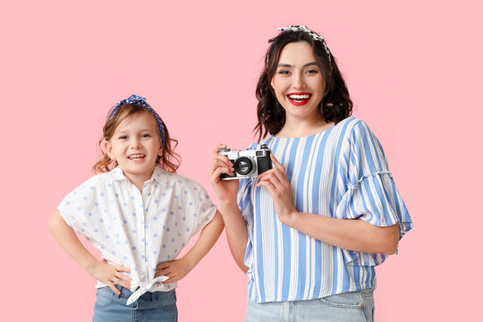 Beautiful pin-up woman with photo camera and her daughter on pink background