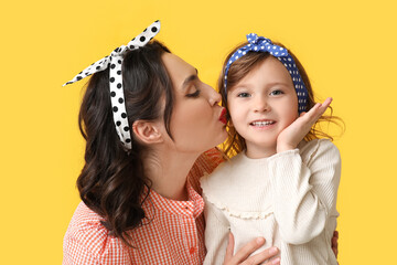 Beautiful pin-up woman kissing her daughter on yellow background - obrazy, fototapety, plakaty