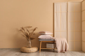 Wooden bench with soft pillows near beige wall