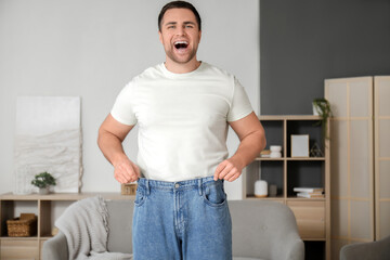 Happy young man in loose jeans at home. Weight loss concept