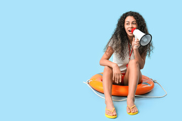 Beautiful young happy African-American female lifeguard with megaphone and ring buoy sitting on...
