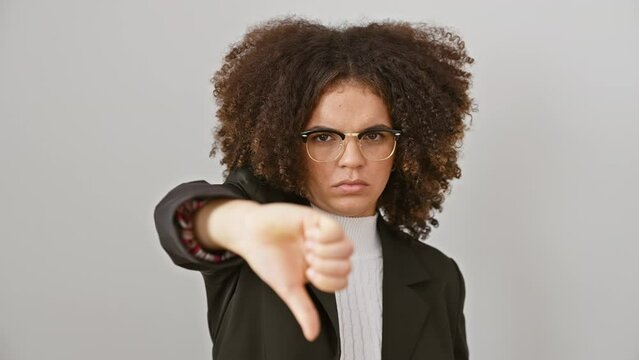 Angry hispanic woman with curly hair showing unbearable disapproval, standing isolated on white background, negative thumb down gesture uncovers her bad mood