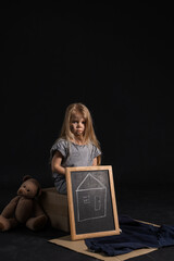 Homeless little girl with picture of house and teddy bear on dark background - obrazy, fototapety, plakaty