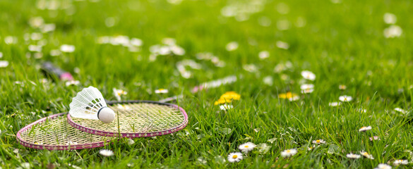 Two badminton rackets and a shuttlecock lie on the green grass.