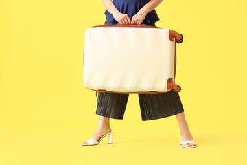 Female traveler with suitcase on yellow background