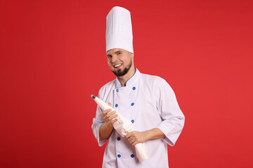 Happy professional confectioner in uniform holding piping bag on red background