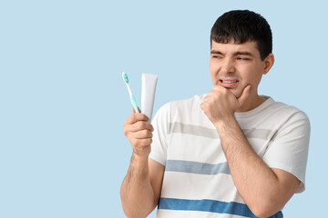 Young man with brush and paste suffering from toothache on blue background