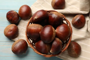 Schilderijen op glas Wicker bowl with roasted edible sweet chestnuts on light blue wooden table, flat lay © New Africa