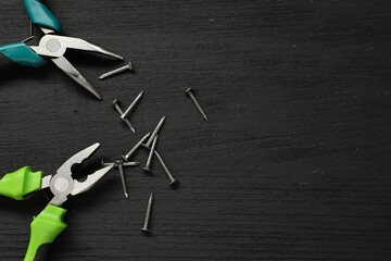 Pliers and nails on black wooden table, flat lay. Space for text