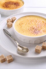 Delicious creme brulee in bowls, sugar cubes and spoon on white wooden table