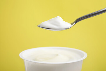 Eating delicious natural yogurt on yellow background, closeup