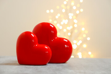 Red ceramic hearts on grey table against blurred lights, space for text