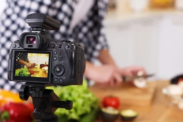 Fotobehang Food blogger cooking while recording video in kitchen, focus on camera © New Africa