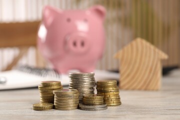 House model, stacked coins and piggy bank on wooden table, selective focus