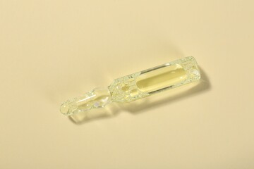 Glass ampoule with liquid on beige background, top view