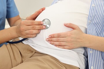 Pregnancy checkup. Doctor with stethoscope listening baby's heartbeat in patient's tummy in clinic,...