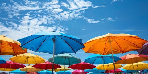 Fototapeta na wymiar Colorful beach umbrellas under blue sky, multiple colors, summer vacation concept, outdoor relaxation theme. Copy space.